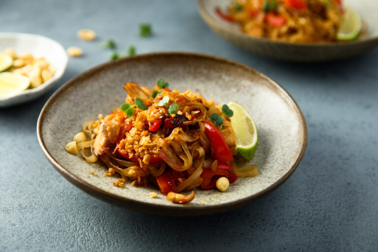 Peanut noodles with crispy tofu on a white plate and blue table surface