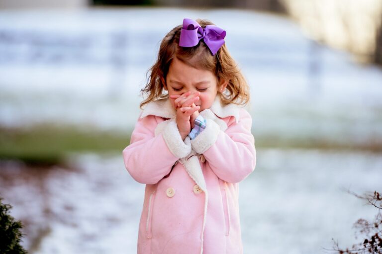 Little girl in pink coat coughing outdoors, to illustrate "my child might have asthma"