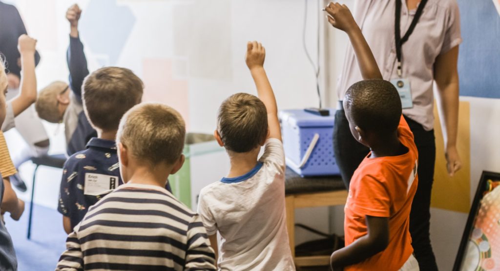 Child at the back of classroom with hand down, when all other hands are up, to illustrate possible social anxiety
