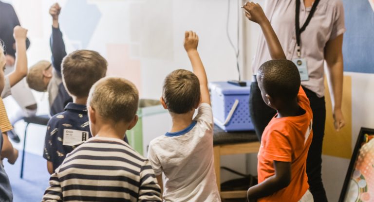 Child at the back of classroom with hand down, when all other hands are up, to illustrate possible social anxiety