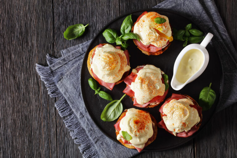 Easy oven-baked eggs Benedict on a black plate with a pitcher of hollandaise