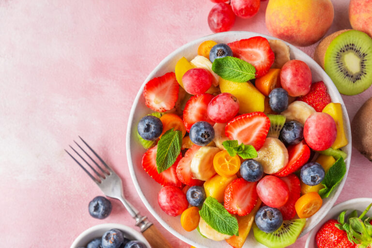 Fruit salad with mint, honey and lime on a pink background