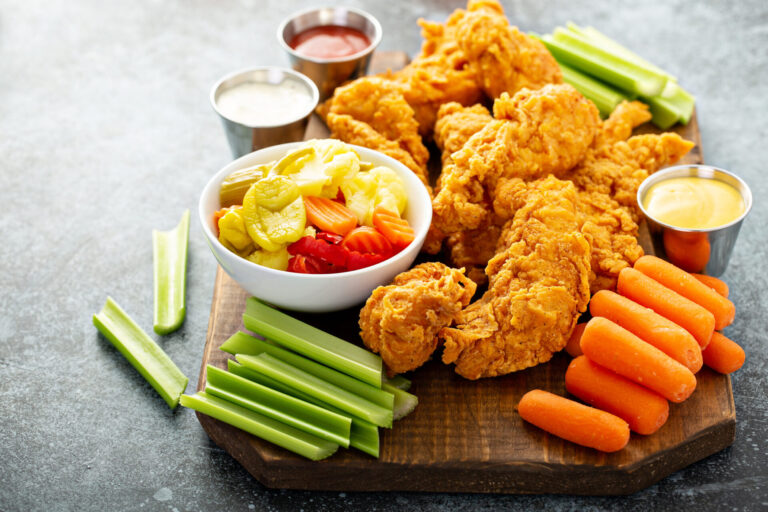 Buttermilk chicken strips with crudités and dip on a wooden serving board