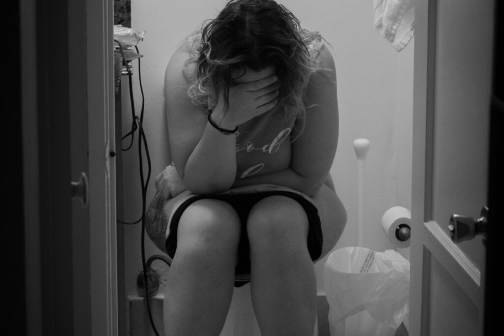 Black and white photo of a woman sitting on the toilet looking upset because she is suffering from infertility