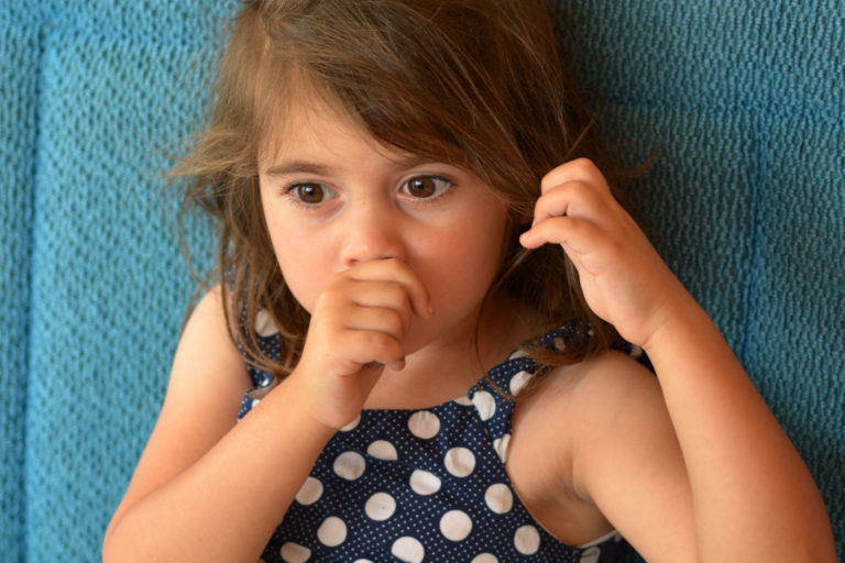 Child in a polka dot shirt sucking thumb and holding ear, to illustrate self-soothing behaviours