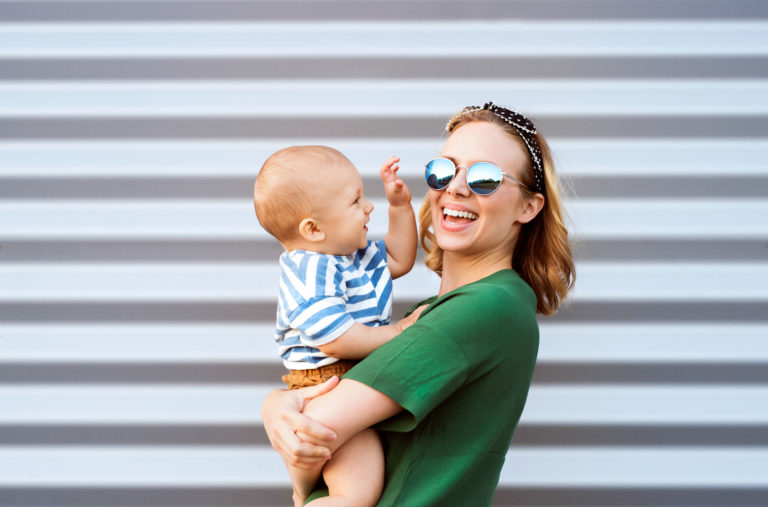 Young woman with a baby boy standing against the wall.