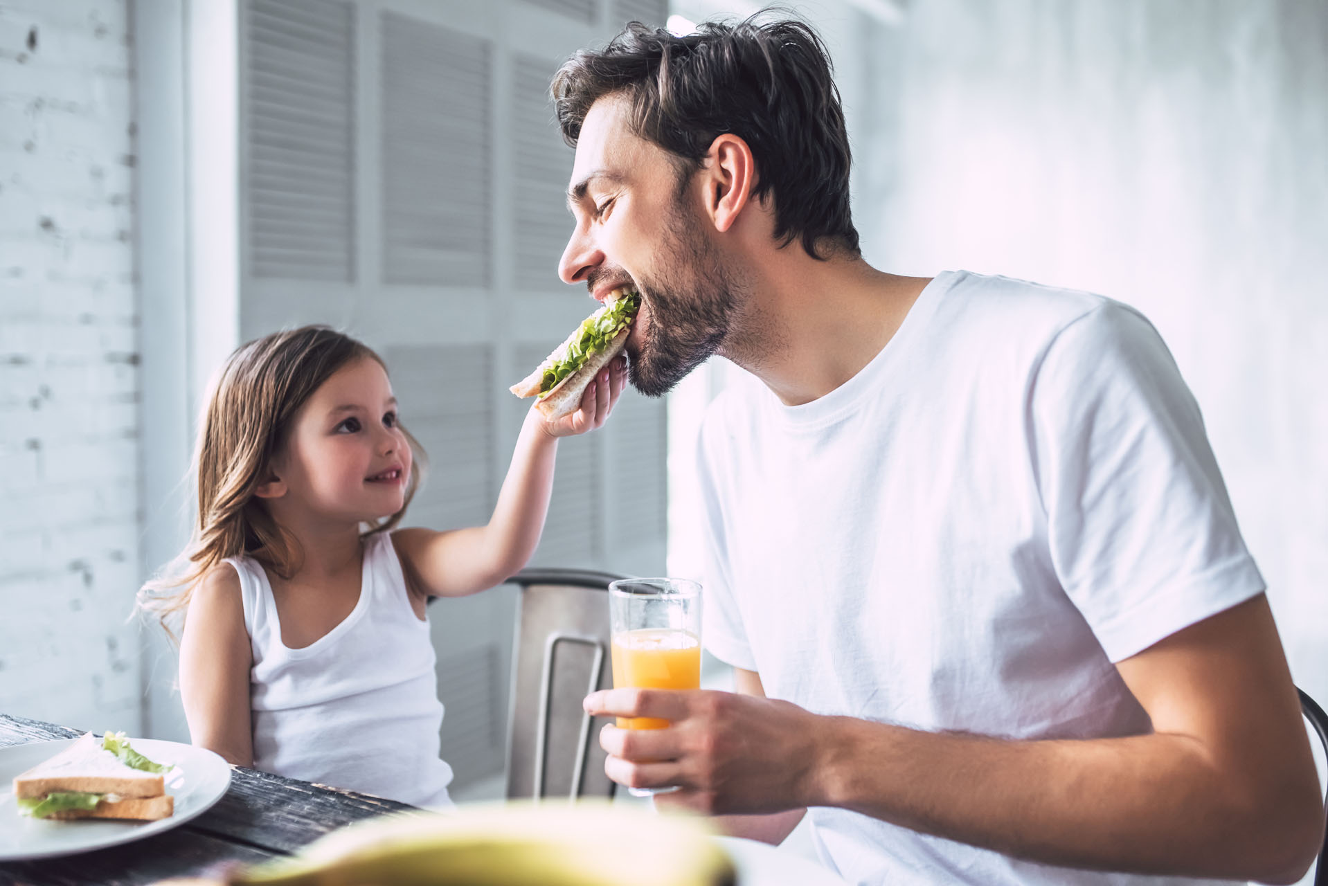 daughter feeding dad a sandwich at the table