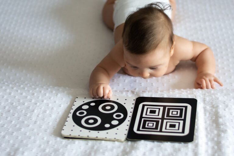 a baby lays on a blanket looking at a contrasting black and white book.