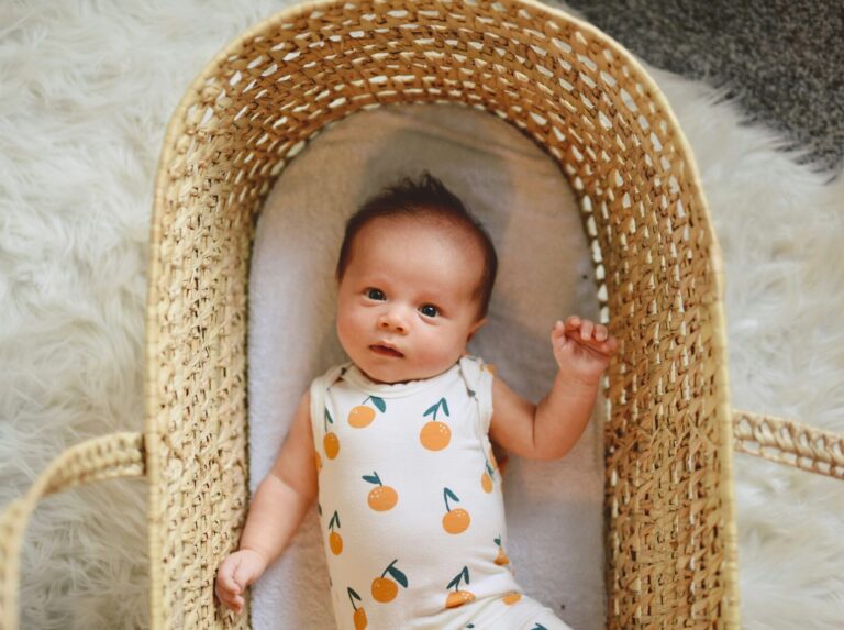 Baby in a peach-printed onesie in a Moses basket, to illustrate popular baby names in Canada in 2025