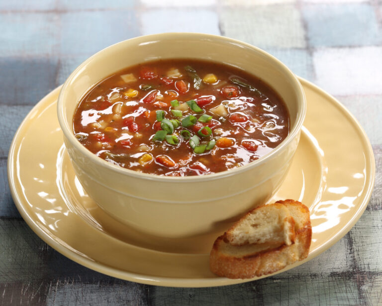 Hamburger soup in a yellow bowl with a saucer and piece of toasted bread on the side