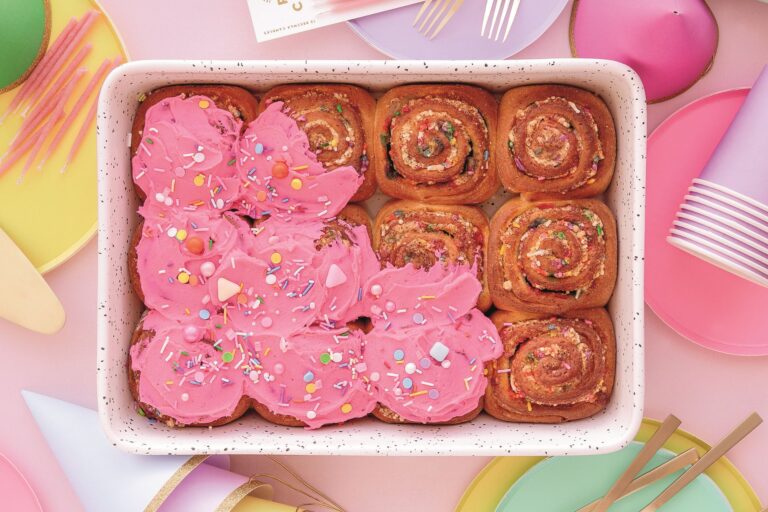 A tray of sprinkle-filled rolls with bright pink frosting