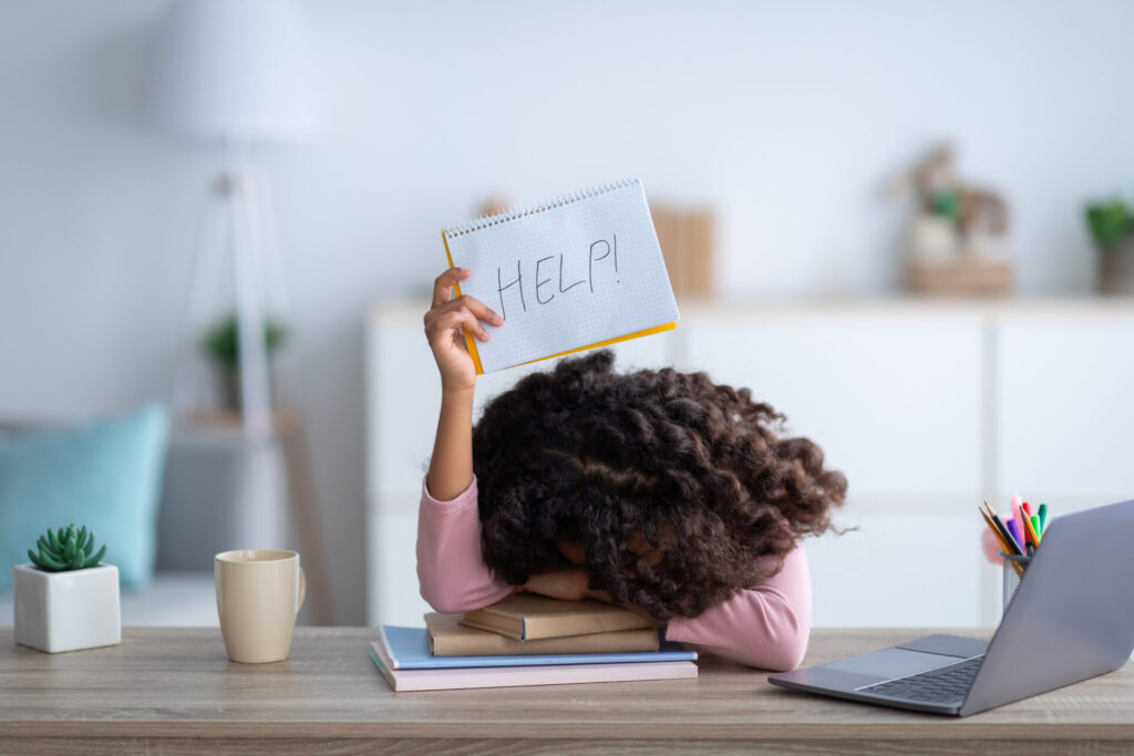 Overwhelmed by work and parenting, Mom with curly black hair holds up a Help sign