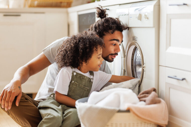 Dad and child loading the washer together, to teach household responsibility
