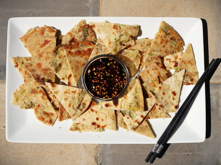 Crispy spring onion pancakes on a rectangular white platter with chopsticks