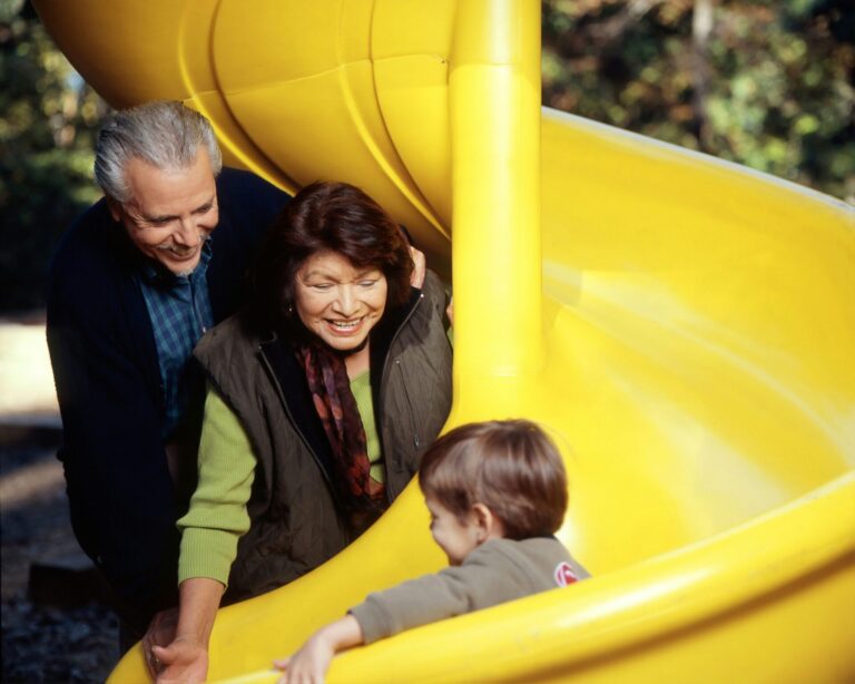 Grandparents watching a child slide down a yellow slide, to illustrate grandparenting styles