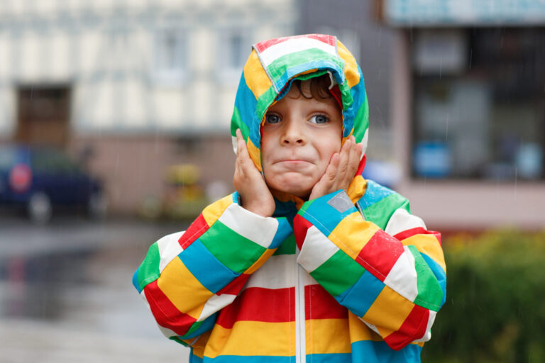 Child in a multicoloured striped coat stuck in the rain, to illustrate natural consequences parenting