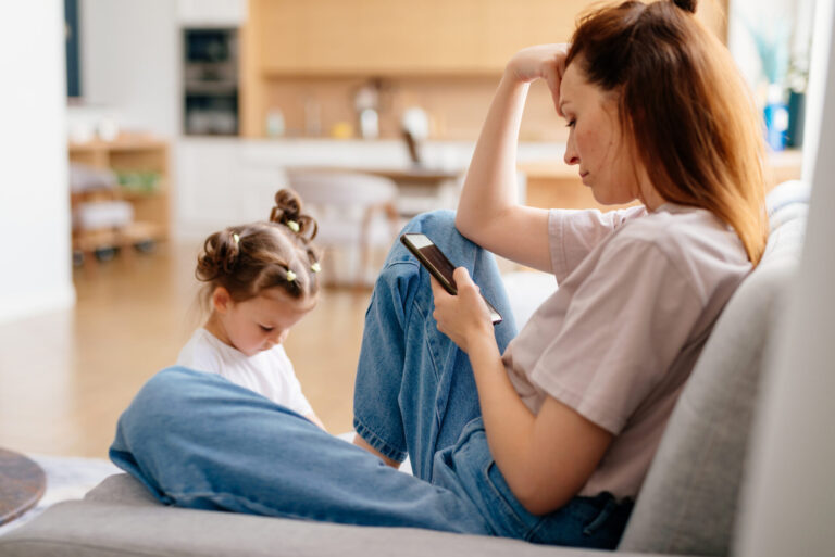 Woman scrolling with child in background, to illustrate parental jealousy